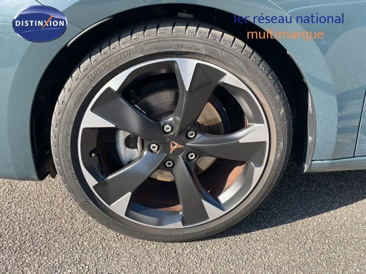 Gros plan sur la roue avant gauche de la CUPRA Leon 1.5 eTSI 150CH DSG en bleu Fjord avec jante alliage noire et grise.