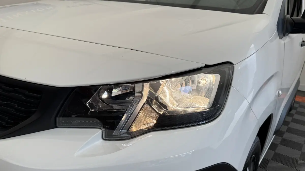 Gros plan sur le phare avant droit du Peugeot Partner blanc, mettant en valeur le design moderne et la calandre noire.