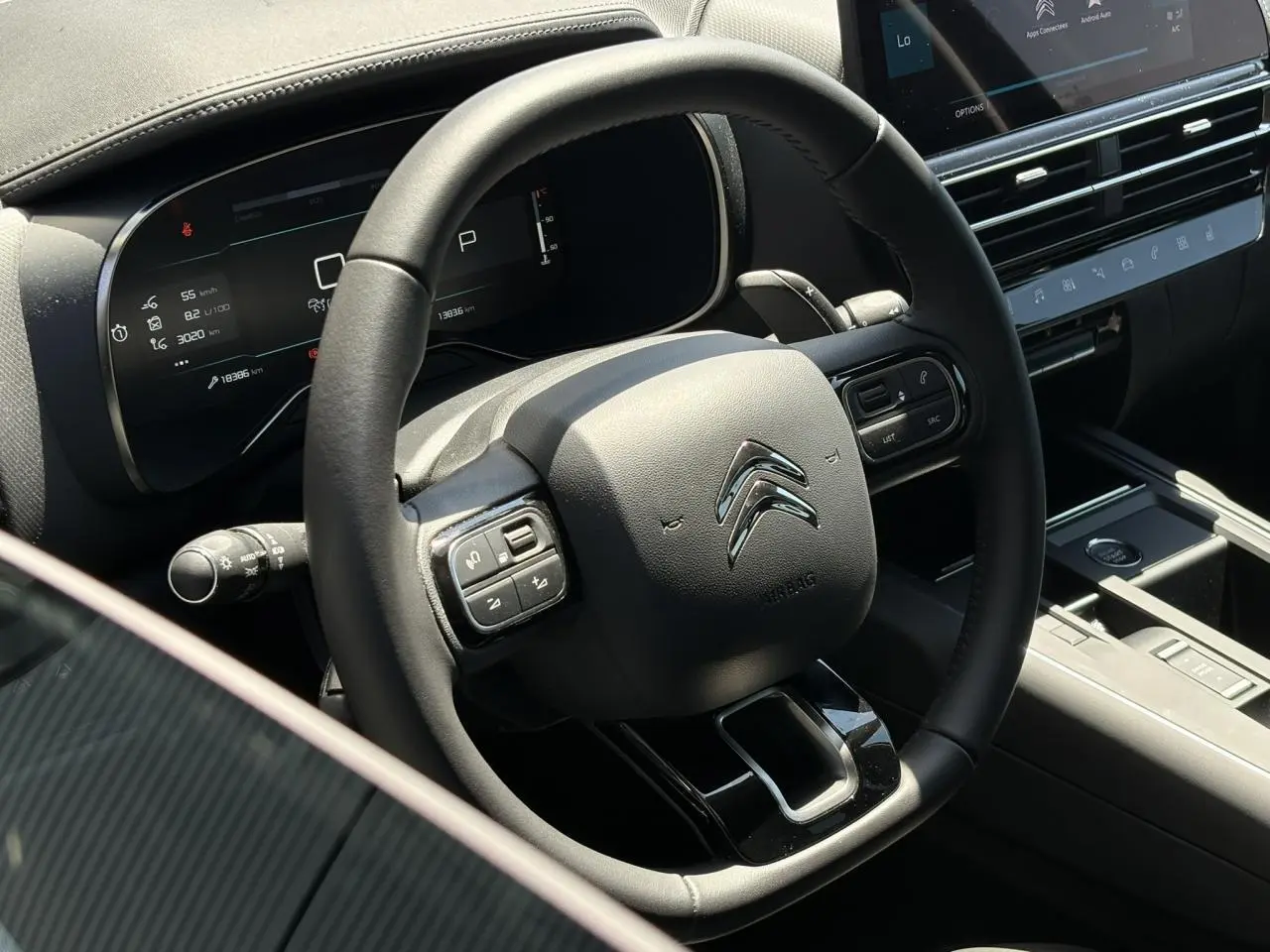 Vue rapprochée du volant noir avec commandes intégrées et tableau de bord numérique du Citroën C5 Aircross Hybrid 2025.
