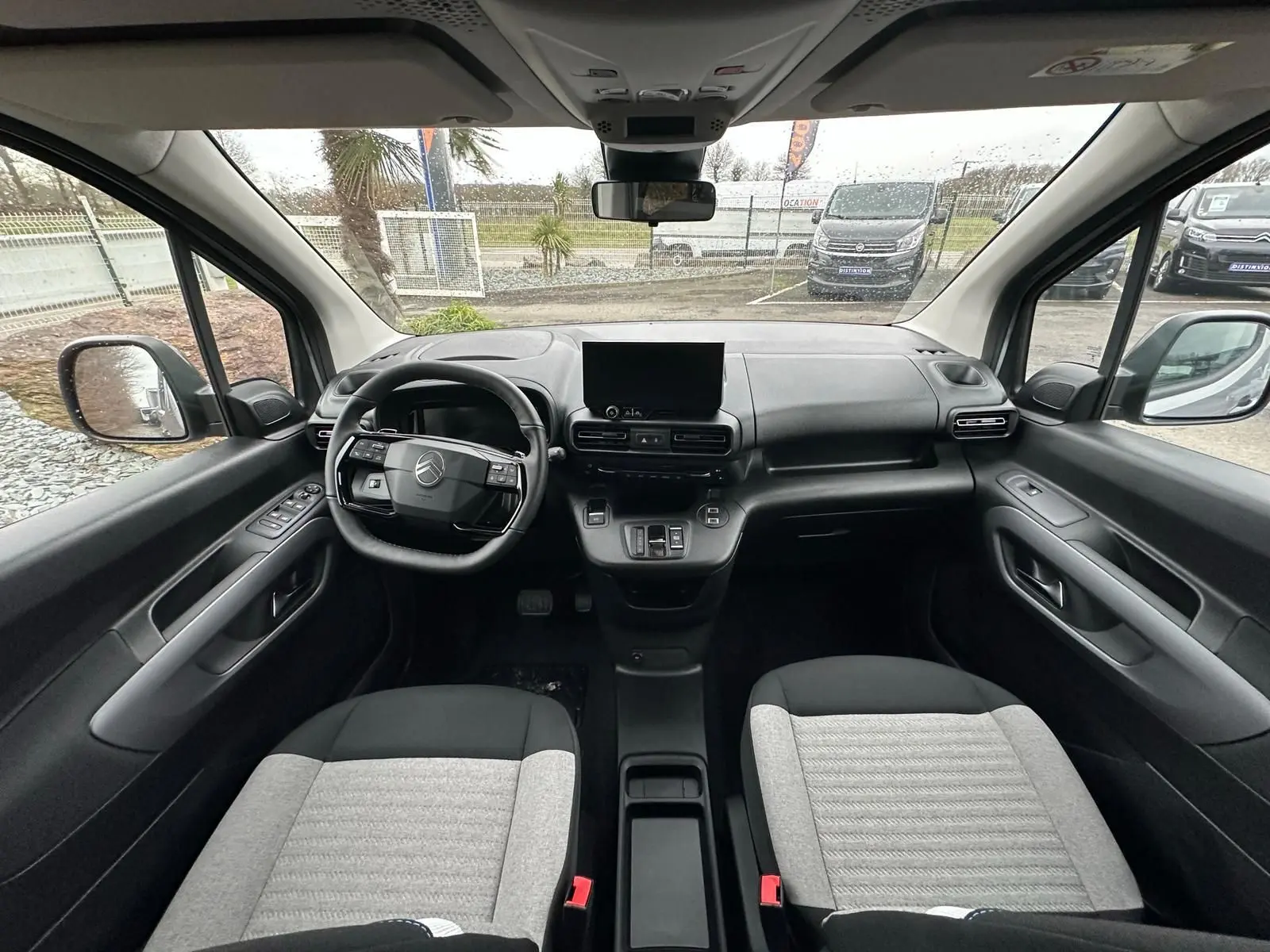 Vue intérieure avant du Citroën Berlingo 2025, sièges bicolores gris et noir, tableau de bord moderne avec écran central.