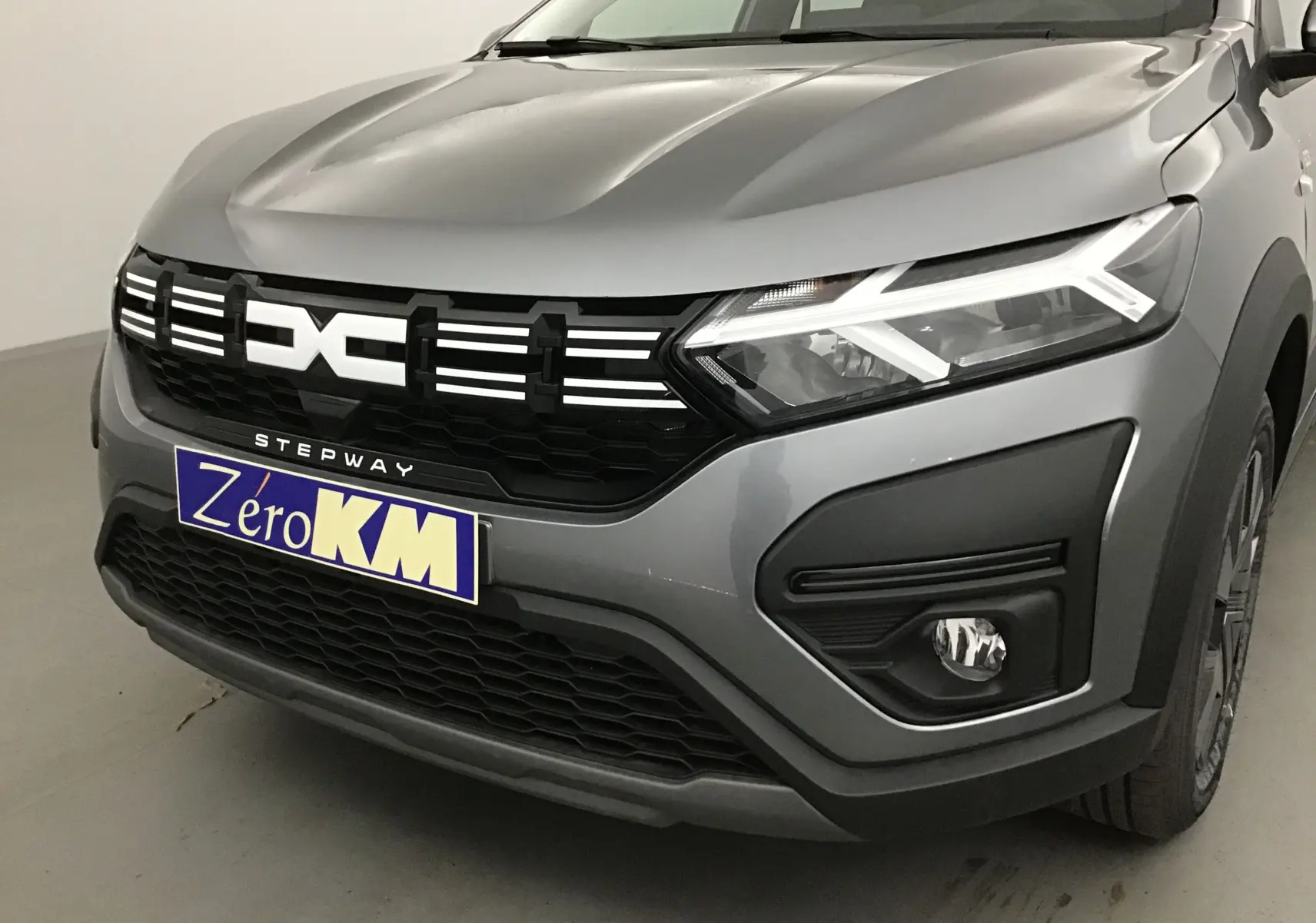 Vue de face droite d'une Dacia Sandero Stepway gris schiste avec calandre noire et éclairage LED distinctif.