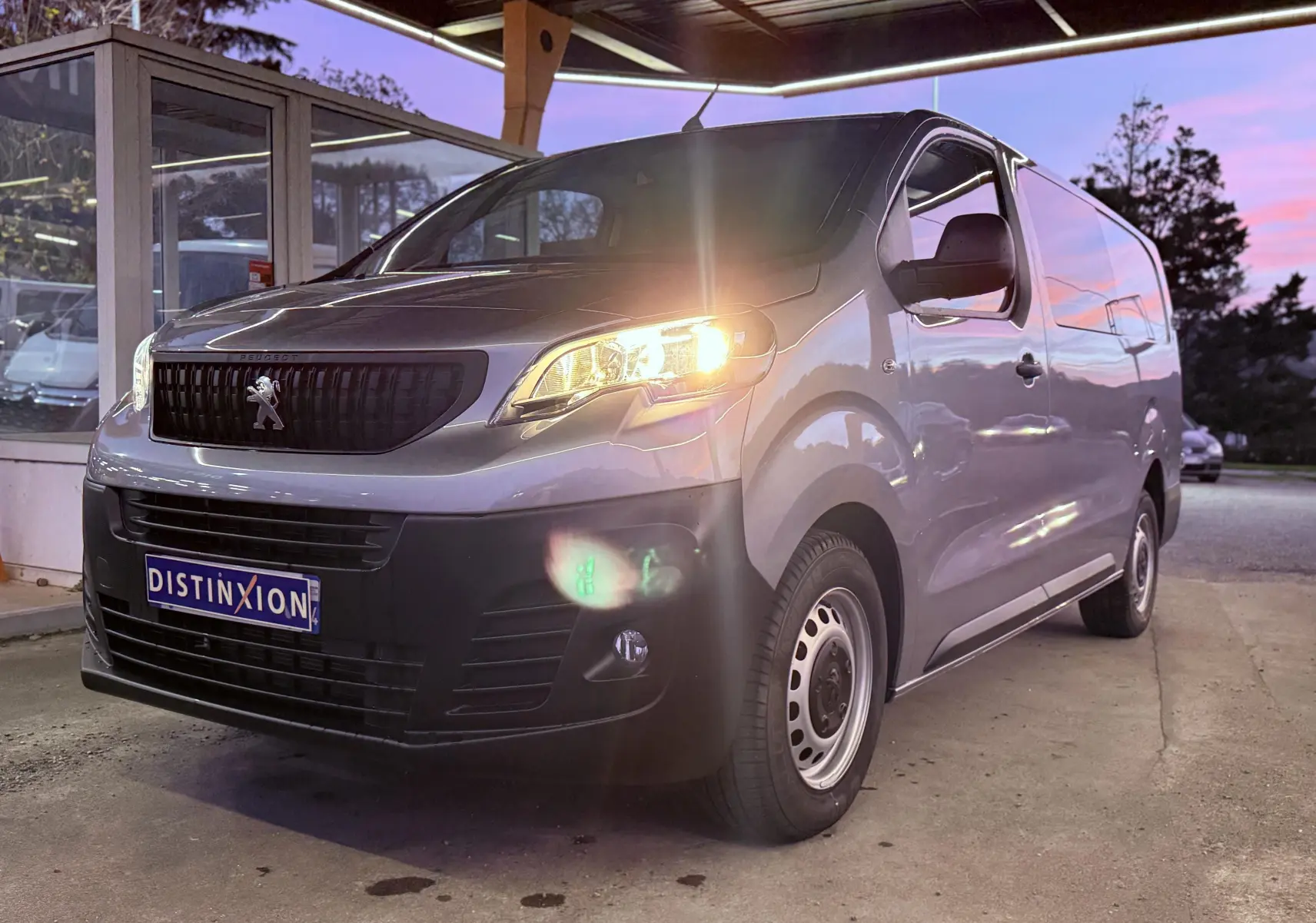 Vue 3/4 avant droit d'un Peugeot Expert Cabine Approfondie gris Artense métal avec phare allumé sous un abri.