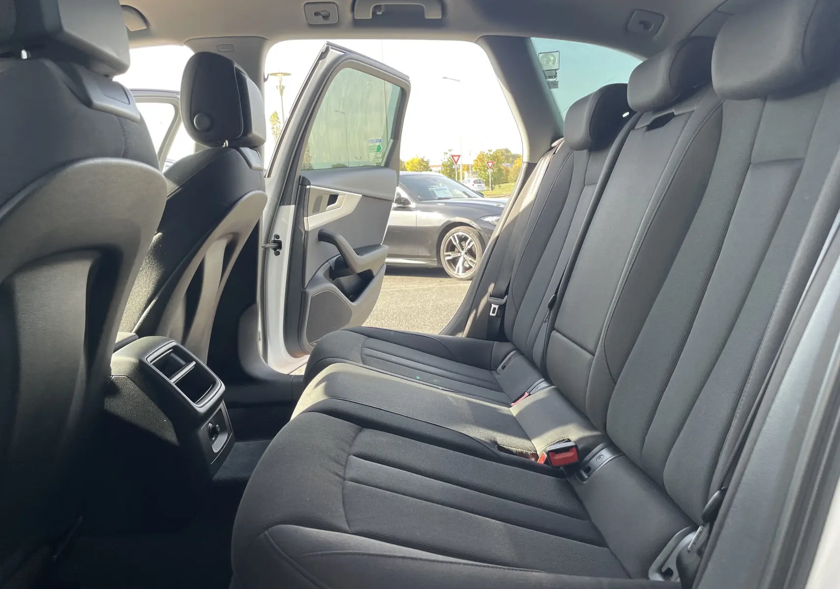 Vue intérieure arrière droite sur les sièges en tissu gris noir d'une Audi A4 Avant blanche avec porte ouverte côté droit.