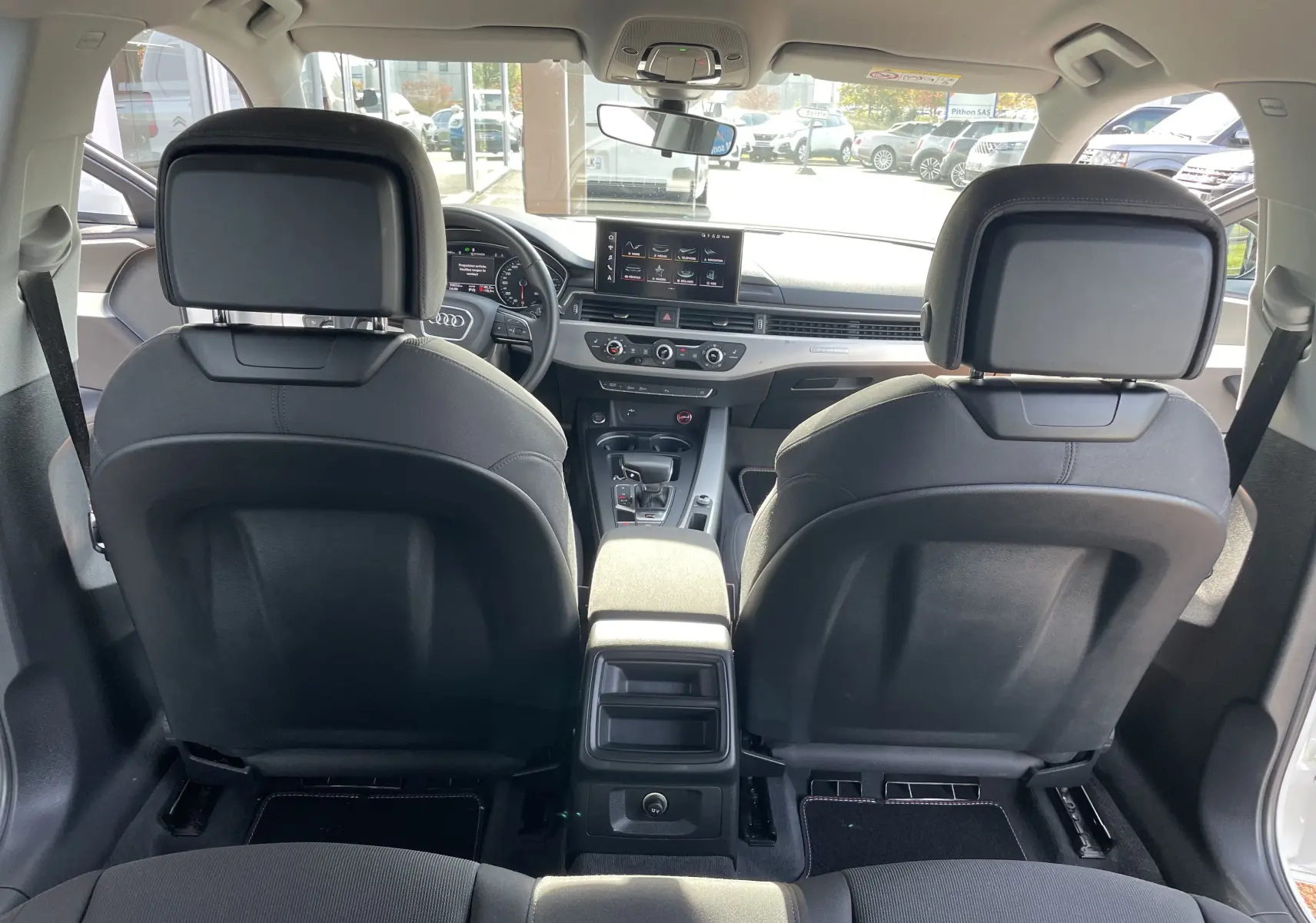 Vue depuis la banquette arrière de l'habitacle gris noir d'une Audi A4 Avant 40 TDI blanc, avec tableau de bord et écran central visibles.