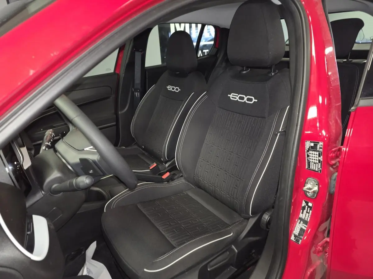 Intérieur côté conducteur d'une FIAT 600 rouge 2024, sièges noirs avec logo 600 brodé et tableau de bord visible.