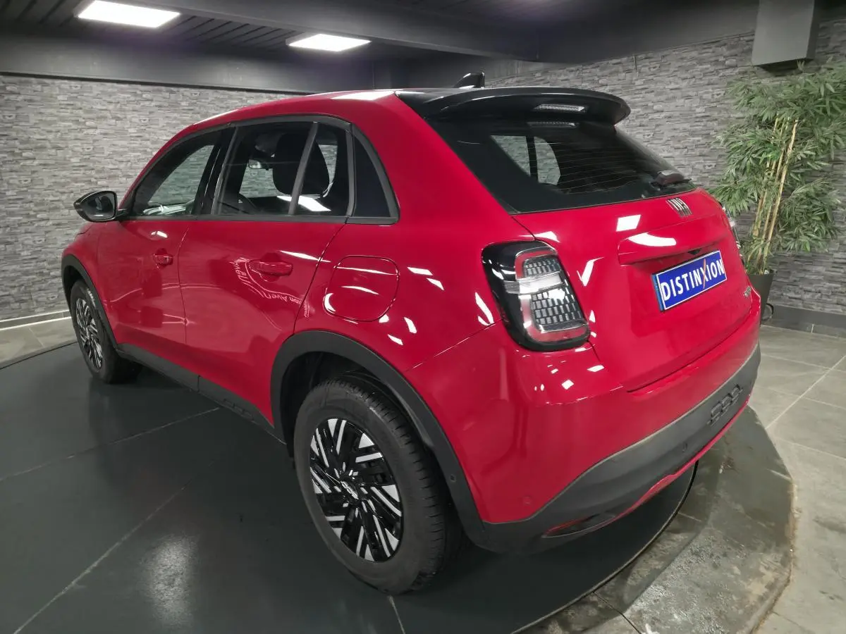 Vue 3/4 arrière droite d'un FIAT 600 rouge avec jantes bicolores et feux arrière LED dans un showroom.