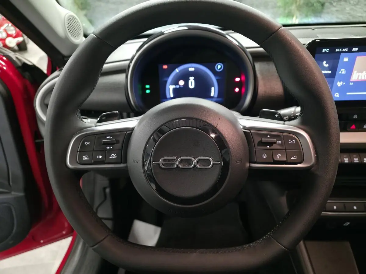 Vue centrée sur le volant noir avec logo 600, tableau de bord numérique et portière rouge visible côté gauche.