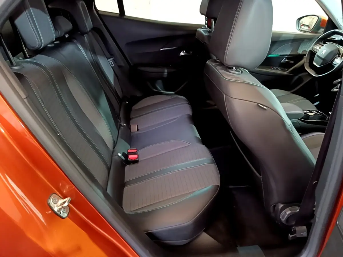 Vue intérieure côté arrière gauche du Peugeot 2008 orange, montrant la banquette arrière et les sièges avant en tissu noir.
