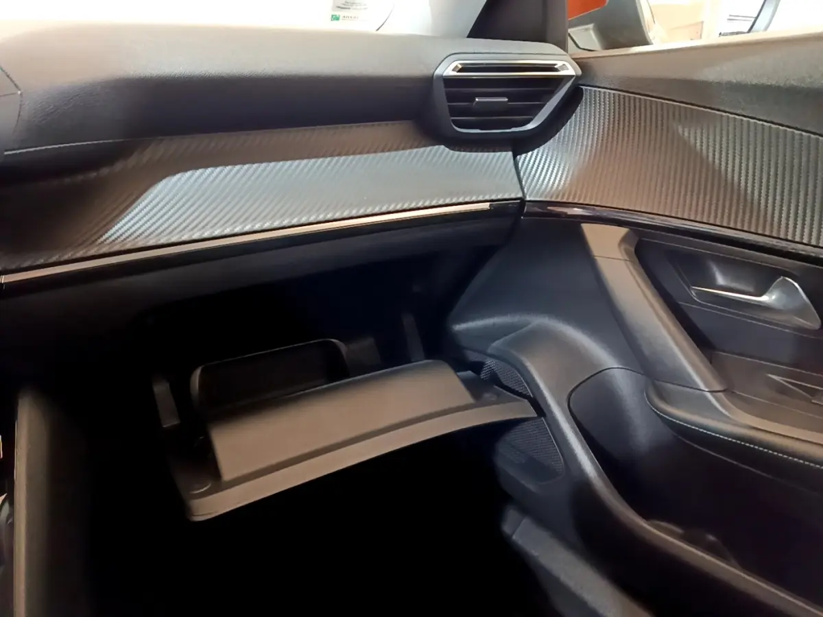 Intérieur côté passager du Peugeot 2008 2021, tableau de bord noir avec finition carbone et boîte à gants ouverte.