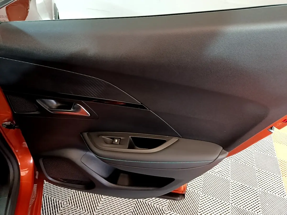 Vue intérieure de la porte côté gauche d'un Peugeot 2008 orange, avec garniture noire et surpiqûres bleues.