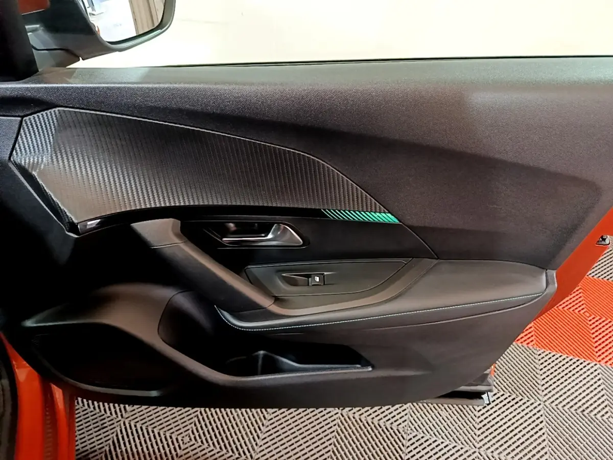 Intérieur côté gauche de la porte avant d’un Peugeot 2008 orange, avec habillage noir et insert décoratif carbone.