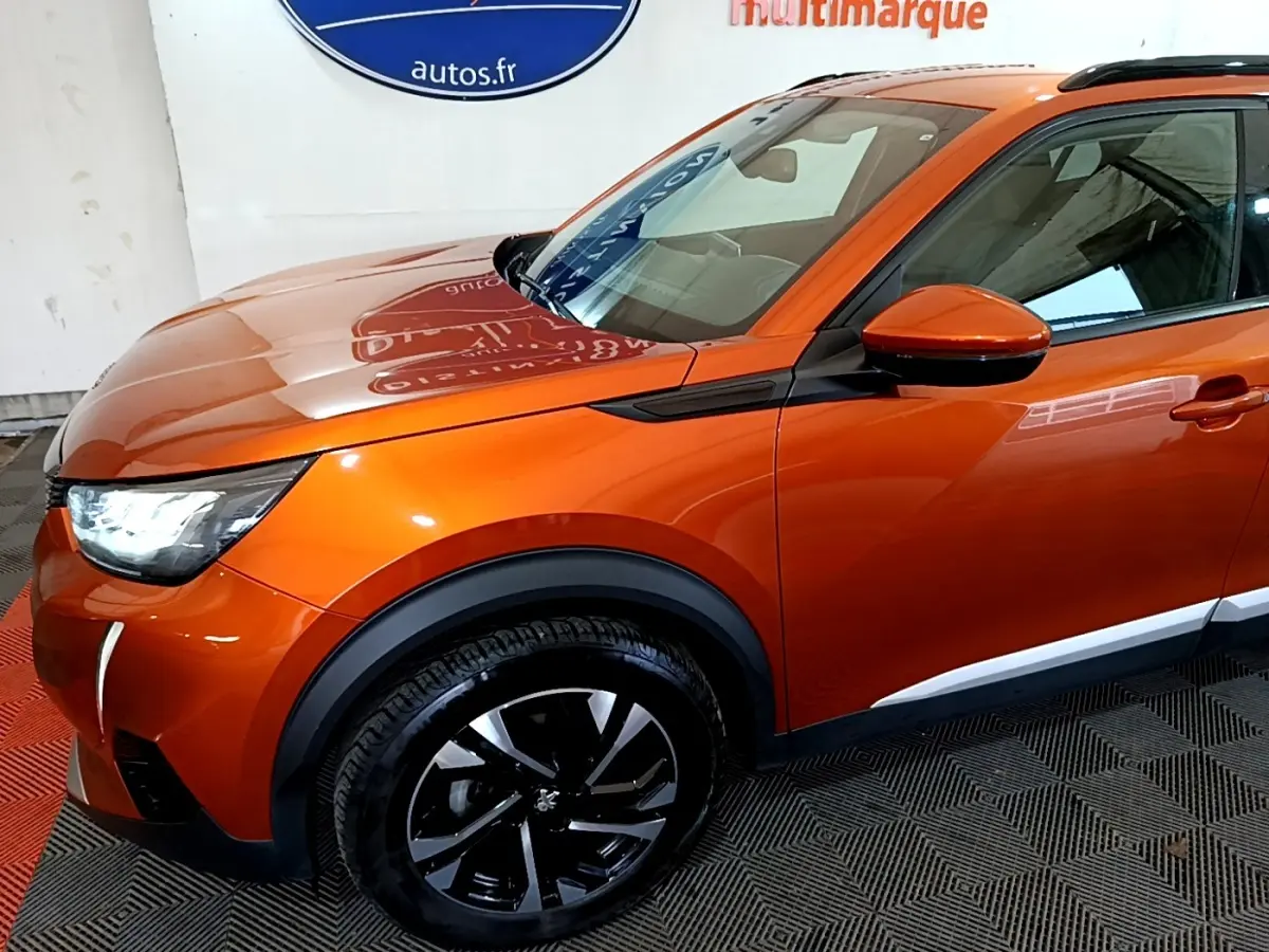 Peugeot 2008 orange vue 3/4 avant droit, avec phares LED allumés et jantes alliage noires distinctives.