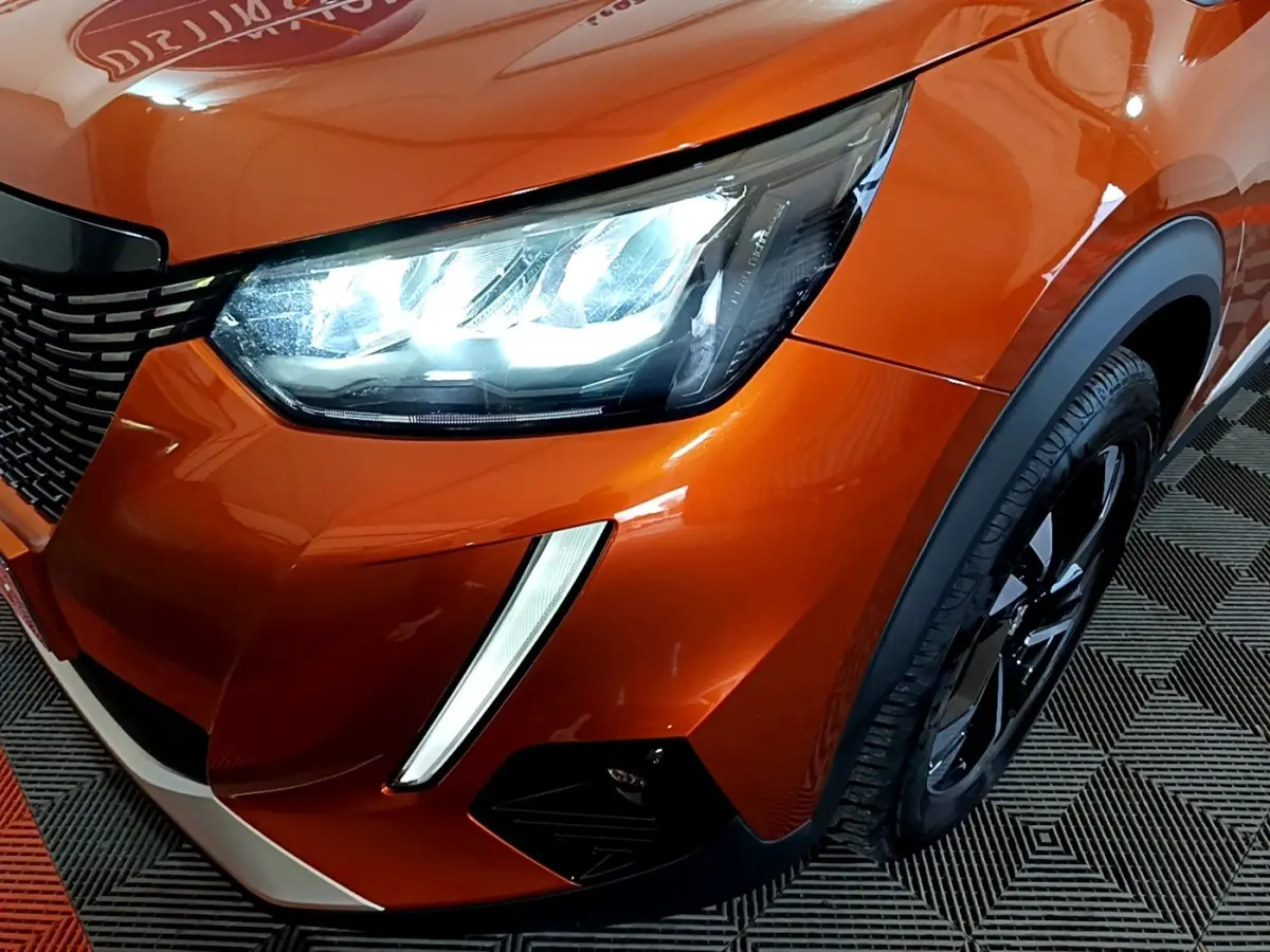 Gros plan sur l'avant droit orange vif du Peugeot 2008 2021, mettant en valeur le phare LED et la calandre noire.