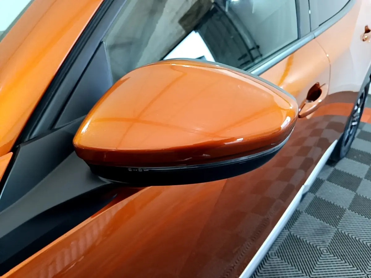 Gros plan sur le rétroviseur côté gauche orange brillant d’un Peugeot 2008 2021, avec partie de la portière visible.