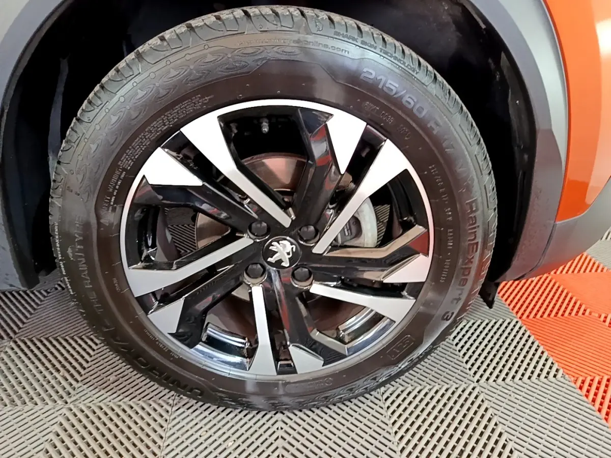 Gros plan sur la roue avant droite du Peugeot 2008 orange, mettant en valeur la jante alliage bicolore et le logo lion.