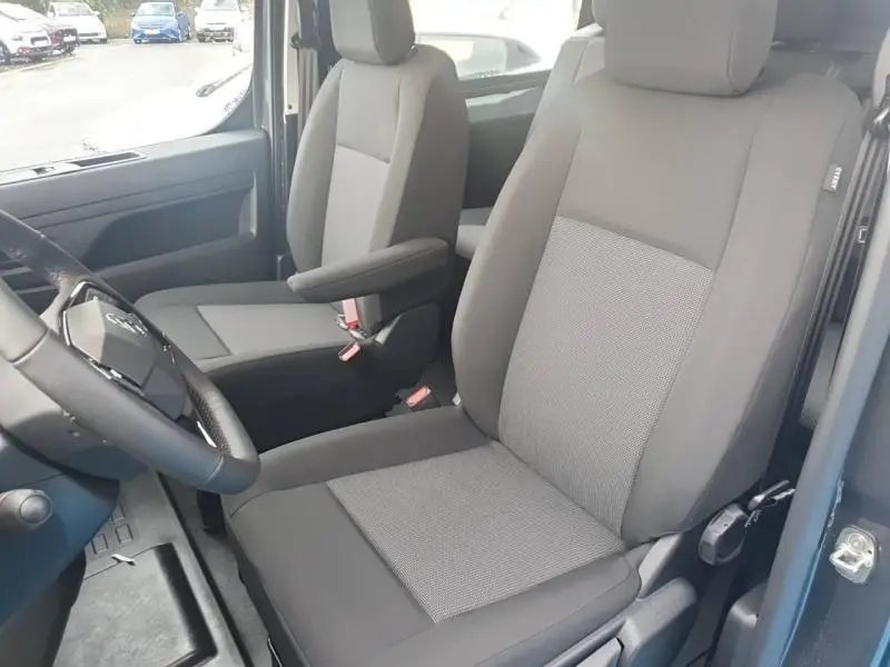 Vue intérieure côté conducteur du Citroën Jumpy 2025, sièges bi-ton gris avec accoudoir et volant cuir.