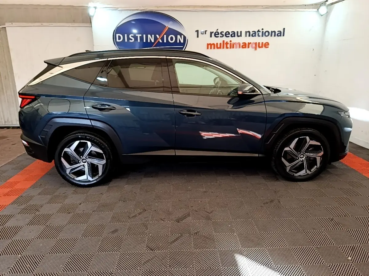 Profil côté droit du Hyundai Tucson bleu 2023 avec jantes alliage et vitres teintées dans un showroom.