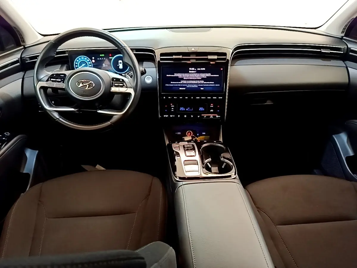 Vue intérieure avant du Hyundai Tucson 2023, tableau de bord noir avec écran tactile central et volant multifonctions.
