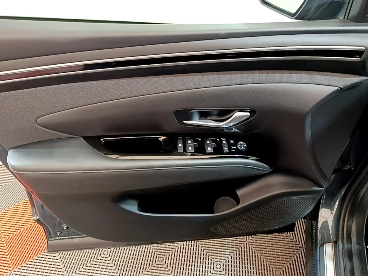 Vue intérieure côté gauche de la porte avant d'un Hyundai Tucson bleu 2023 avec commandes de vitres et poignée argentée.
