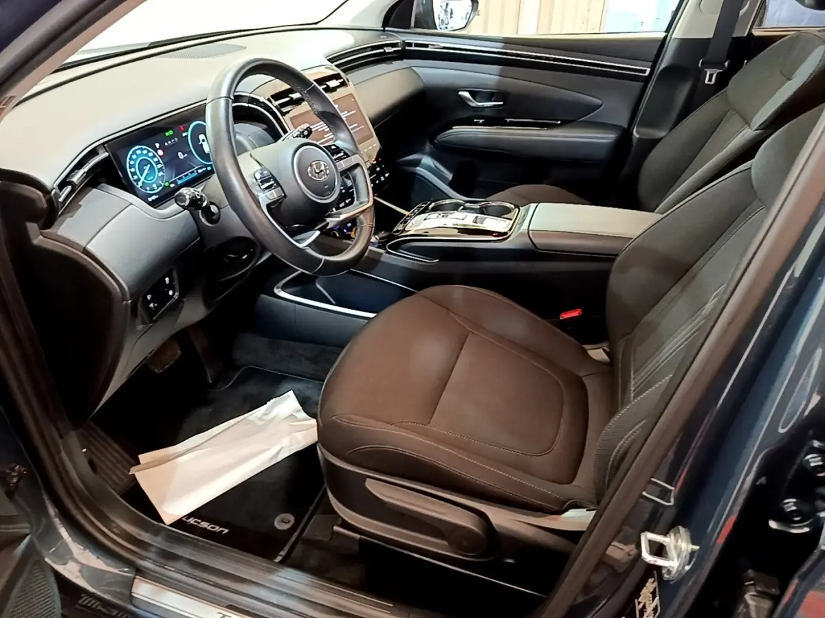 Vue intérieure côté conducteur du Hyundai Tucson bleu 2023, mettant en valeur le tableau de bord digital et la sellerie noire.