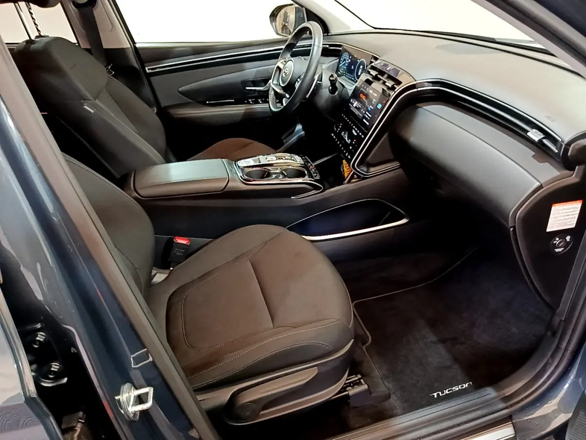 Vue intérieure côté conducteur du Hyundai Tucson bleu 2023, avec tableau de bord digital et console centrale moderne.