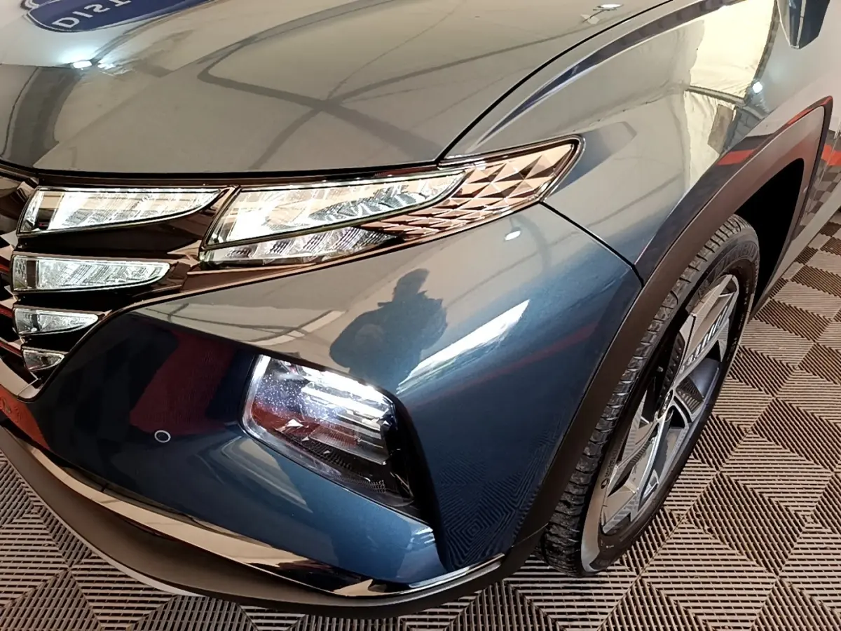Vue rapprochée avant droite du Hyundai Tucson bleu 2023, mettant en valeur ses phares LED et la calandre distinctive.