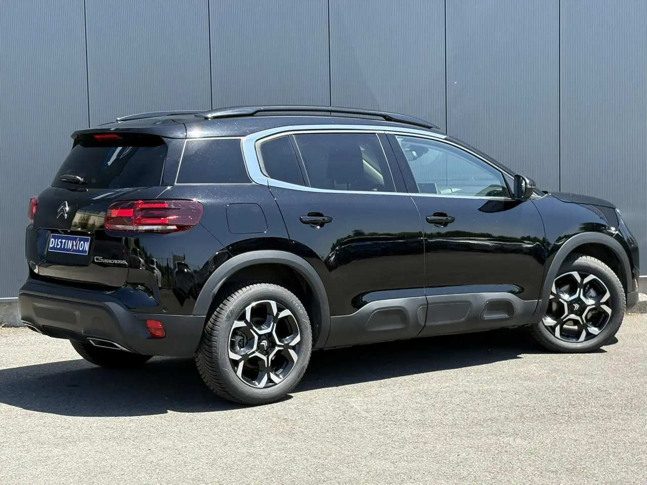 Vue 3/4 arrière droite d'un Citroën C5 Aircross Hybrid 145 noir Perla avec jantes alliage et barres de toit noires.