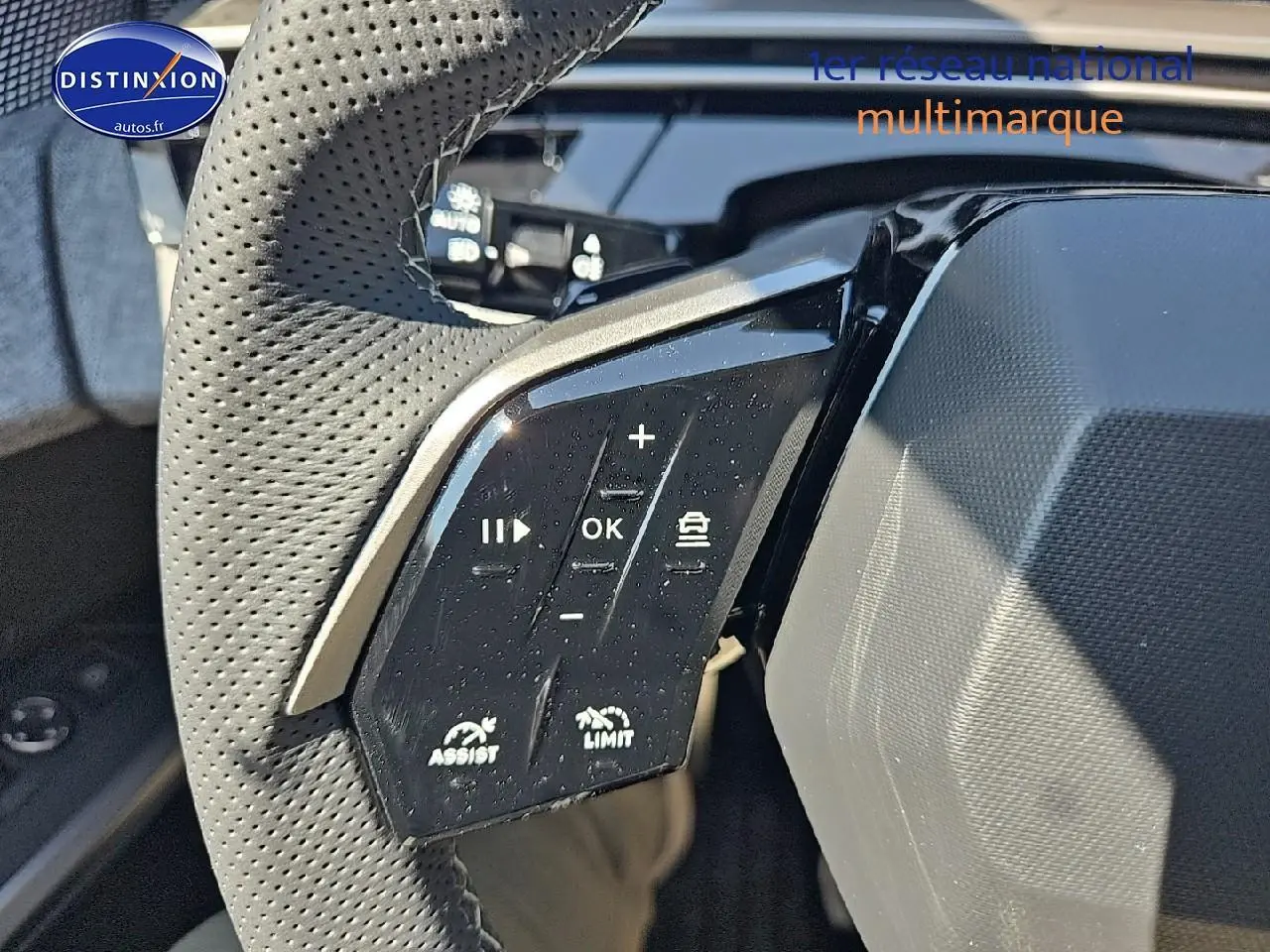Gros plan sur les commandes du volant cuir perforé du Peugeot 5008 Hybrid 145 GT gris titane 2025.