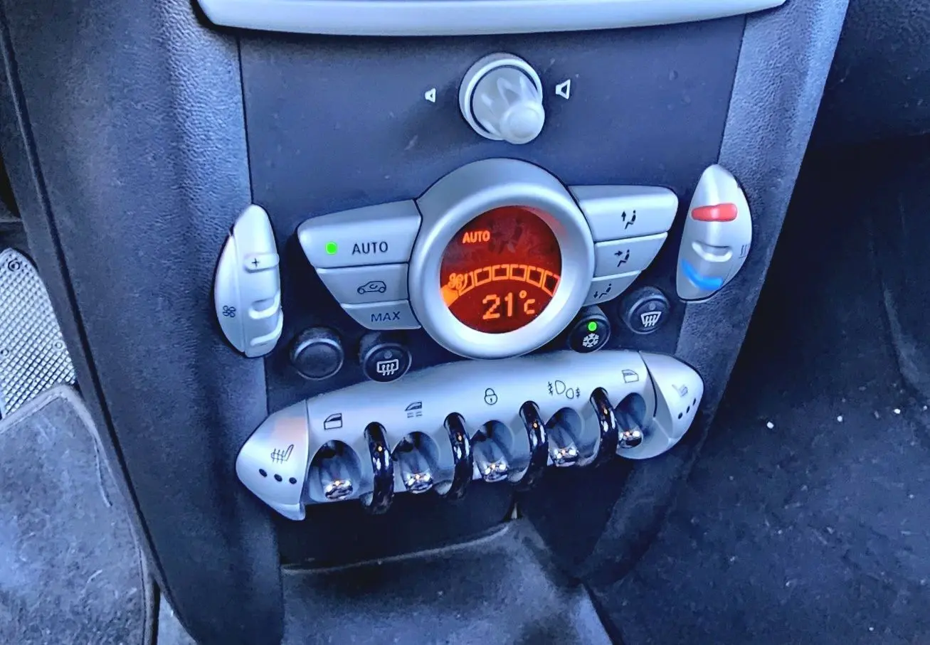 Détail de la console centrale du MINI Cabriolet R57 grise de 2010, affichant la climatisation à 21°C et commandes en chrome.