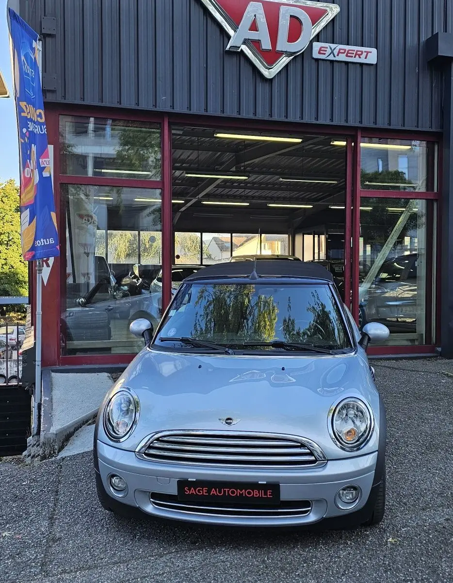 Vue de face d'une MINI Cabriolet R57 grise stationnée devant un garage avec toit noir et logo AD Expert visible.