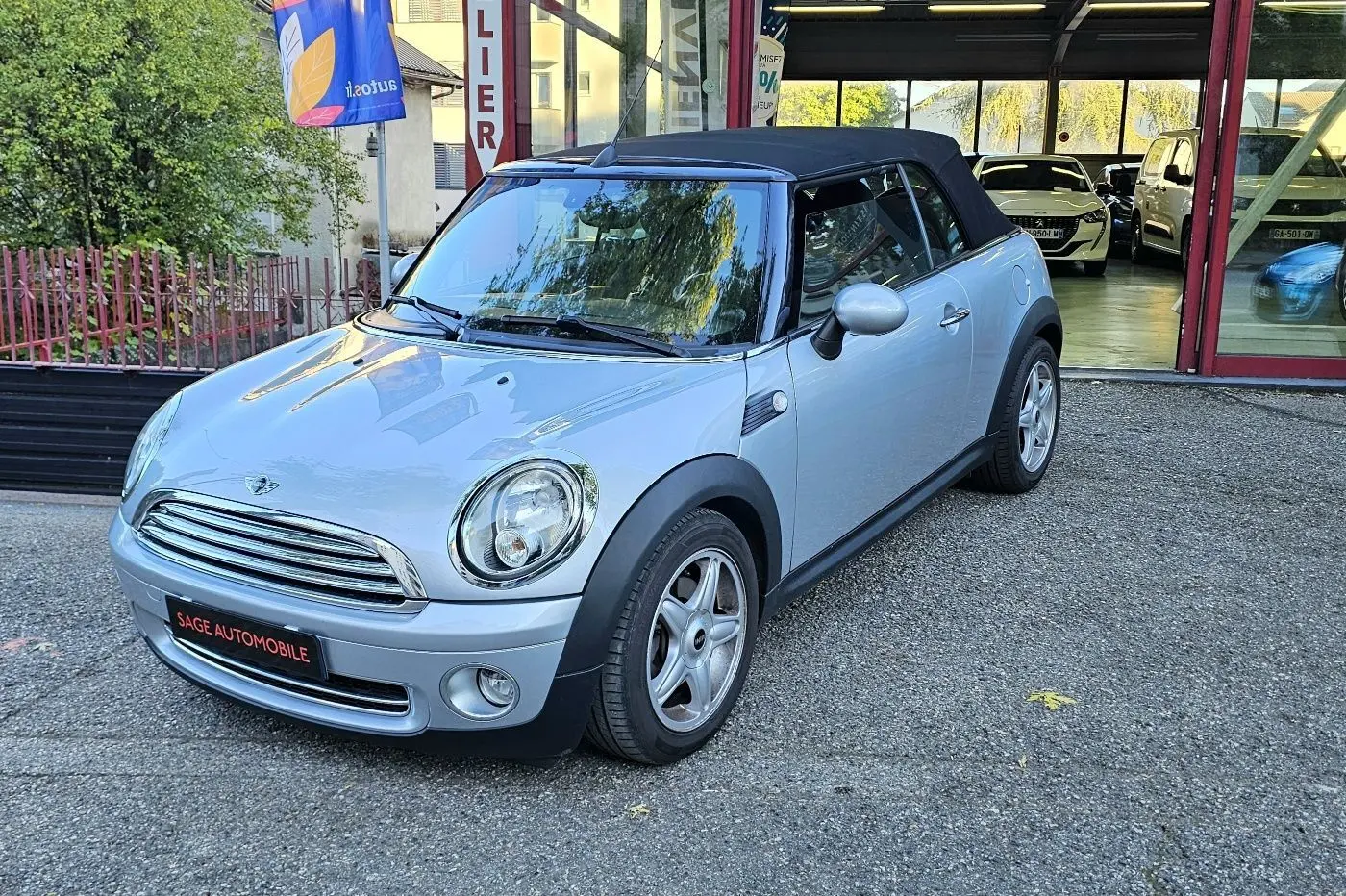 Mini Cabriolet R57 grise vue 3/4 avant droit avec toit noir relevé, stationnée devant un garage.