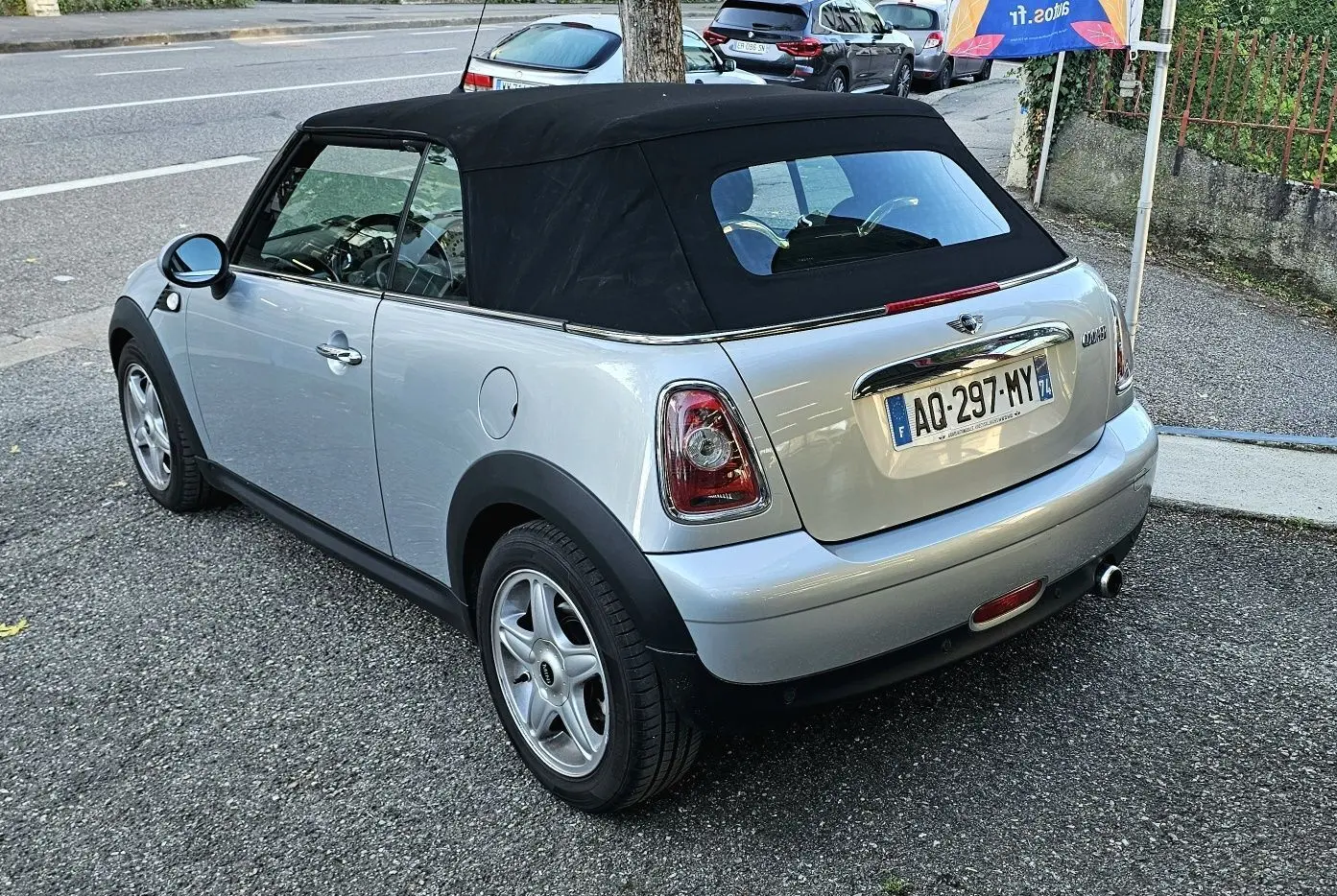 Vue 3/4 arrière droite d'une MINI Cabriolet R57 grise avec capote noire, jantes alliage et échappement chromé visible.
