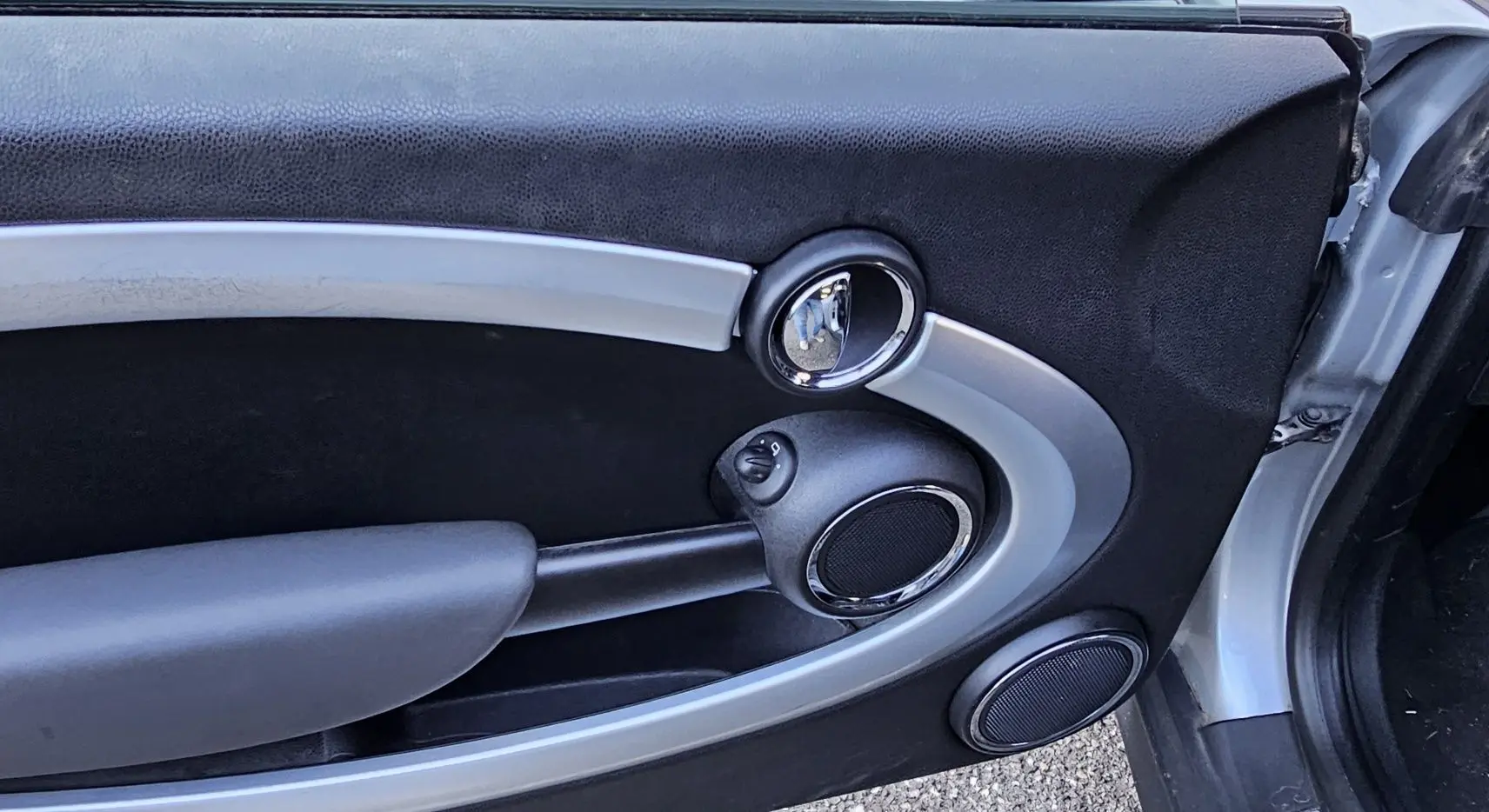 Intérieur de la porte côté gauche d'une MINI Cabriolet R57 grise, avec poignée chromée et haut-parleurs intégrés.
