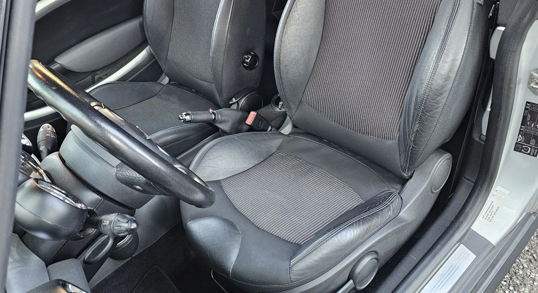 Intérieur côté conducteur d'une MINI Cabriolet R57 grise de 2010, sièges en cuir noir et tissu, volant et frein à main visibles.