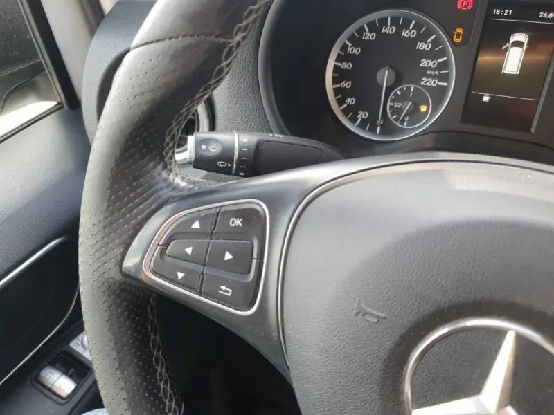 Gros plan sur le volant en cuir perforé et le tableau de bord du Mercedes Vito Fourgon blanc, avec commandes multifonctions visibles.