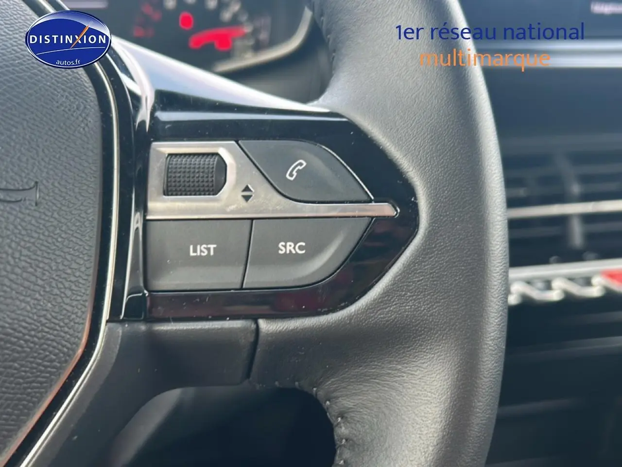Gros plan sur les commandes audio au volant noir du Peugeot 208 1.2 100 style, intérieur moderne avec tableau de bord flou.