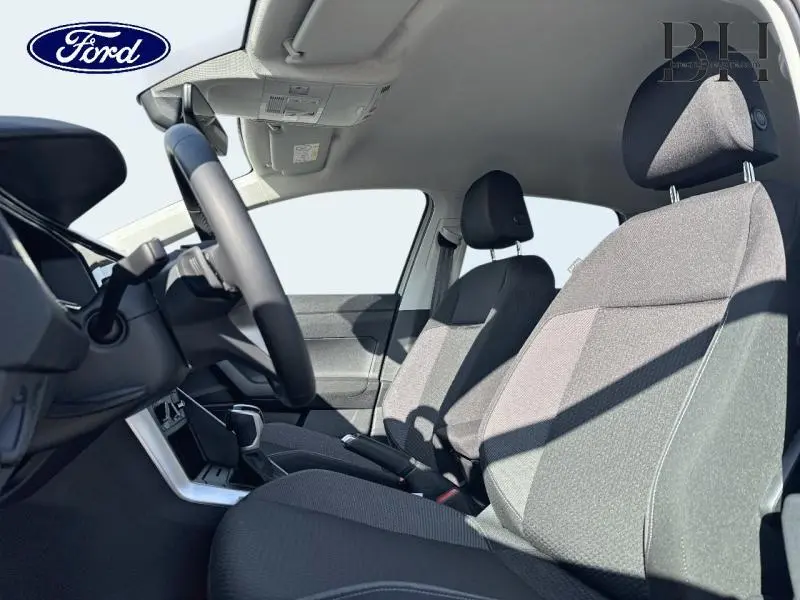 Vue intérieure côté conducteur montrant les sièges tissu gris et le volant multifonction d'un Volkswagen Taigo blanc.