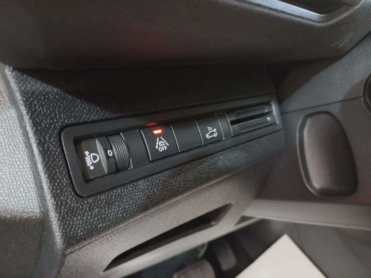 Gros plan sur les commandes d'assistance et réglage des phares côté gauche du tableau de bord noir du Peugeot 5008 gris foncé.