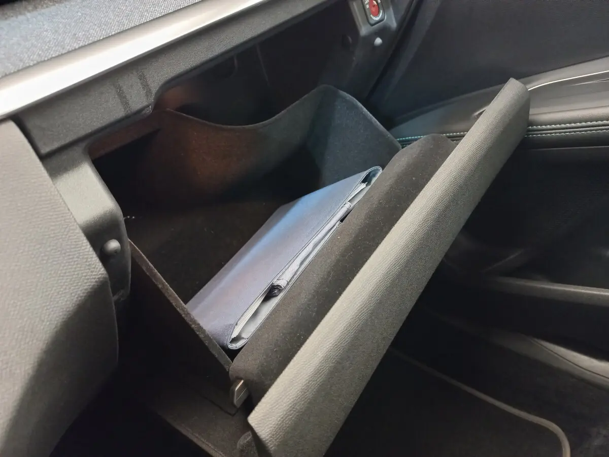 Gros plan sur la boîte à gants ouverte côté passager du Peugeot 5008 gris foncé, avec un manuel à l'intérieur.