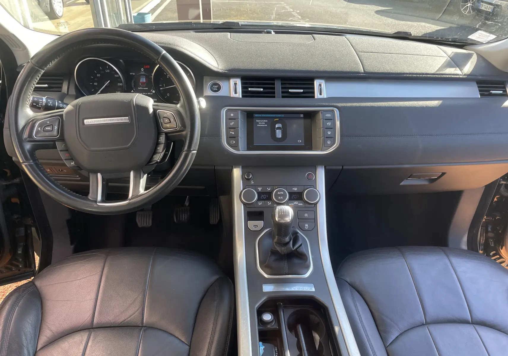 Vue intérieure avant du Range Rover Evoque noir de 2016, montrant le volant, la console centrale avec boîte manuelle et l’écran tactile.