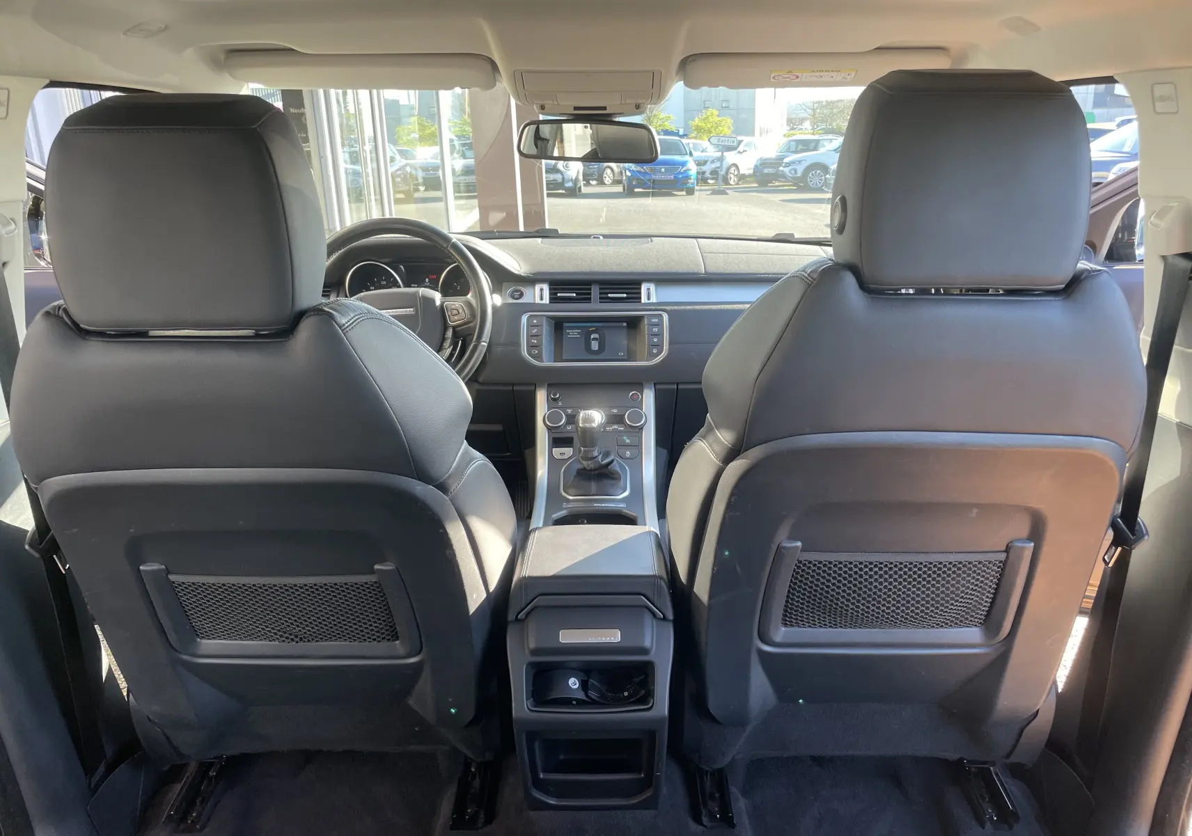 Vue intérieure arrière du Range Rover Evoque noir 2016, montrant les sièges avant en cuir et la console centrale avec boîte manuelle.