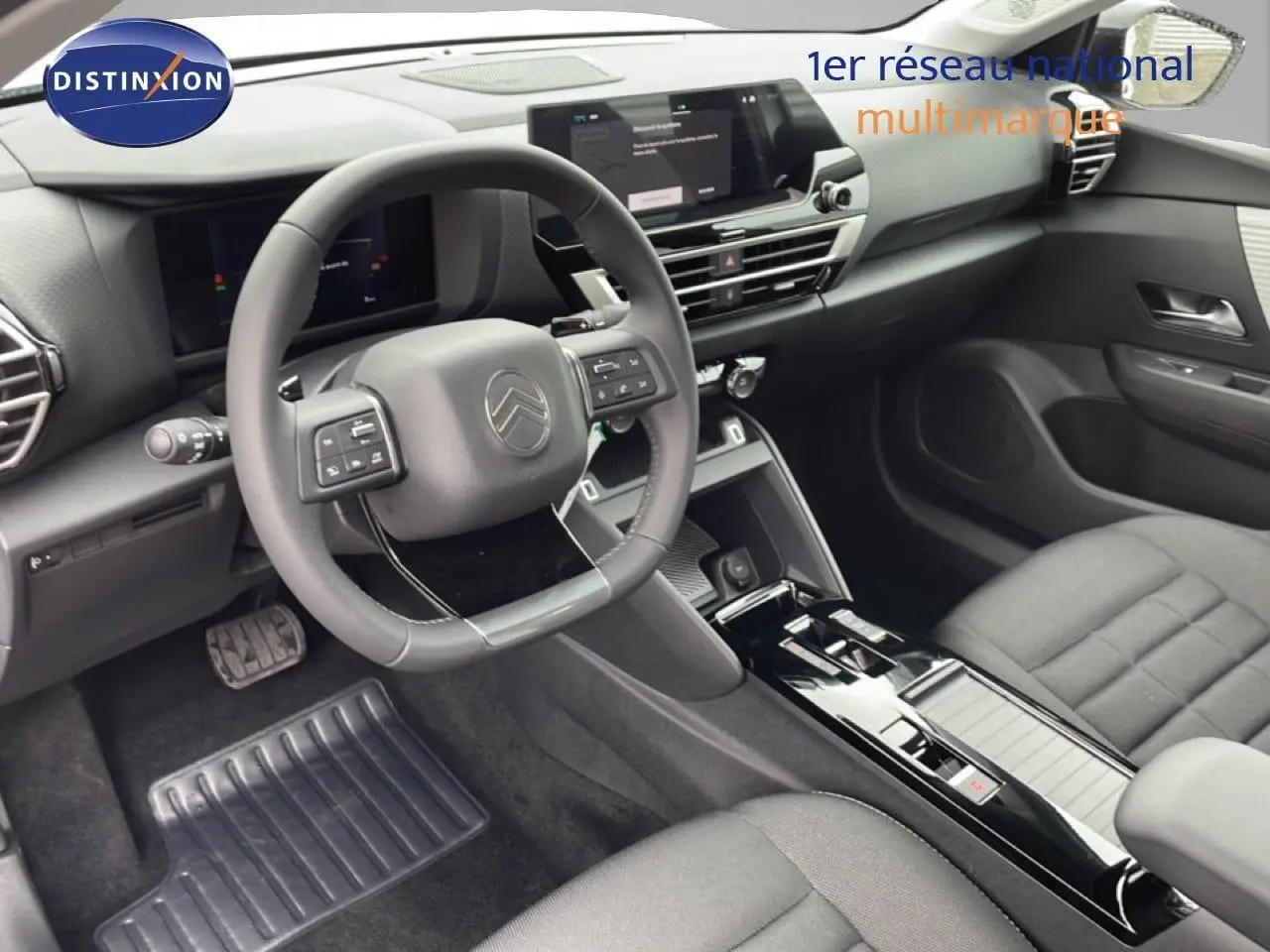 Vue intérieure côté conducteur de la Citroën C4 2026 blanche métal, avec tableau de bord noir et volant multifonction.
