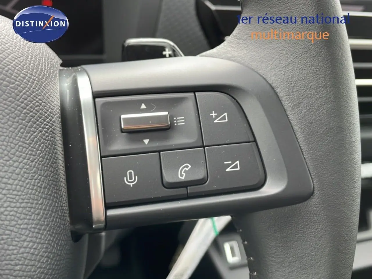 Gros plan sur les commandes du volant en cuir noir d'une Citroën C4 blanche, avec boutons de volume et téléphone.