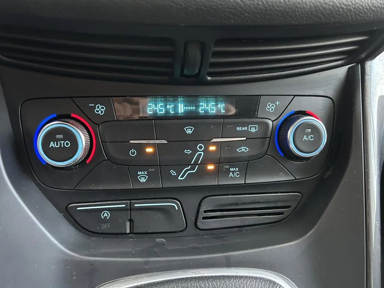 Panneau de climatisation bi-zone avec réglages à boutons rotatifs bleus et rouges dans une Ford C-MAX blanche vue de face.