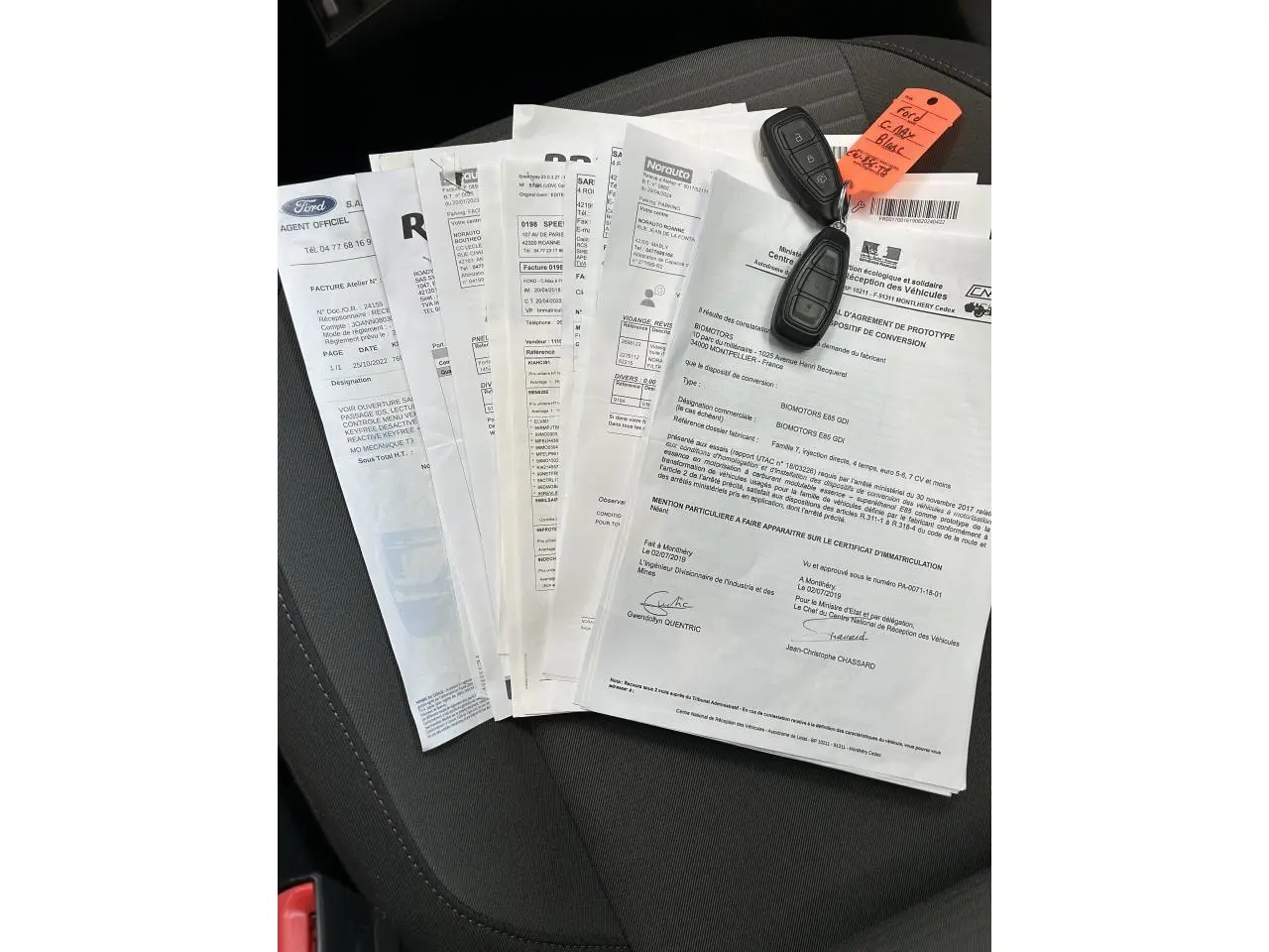 Clé de voiture Ford C-MAX blanche posée sur plusieurs documents sur un siège intérieur noir.