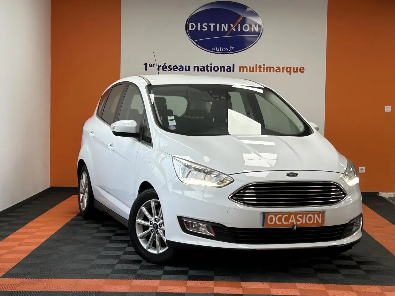 Vue 3/4 avant d'une Ford C-MAX blanche 2018 avec calandre chromée et jantes alliage 16 pouces en intérieur showroom.