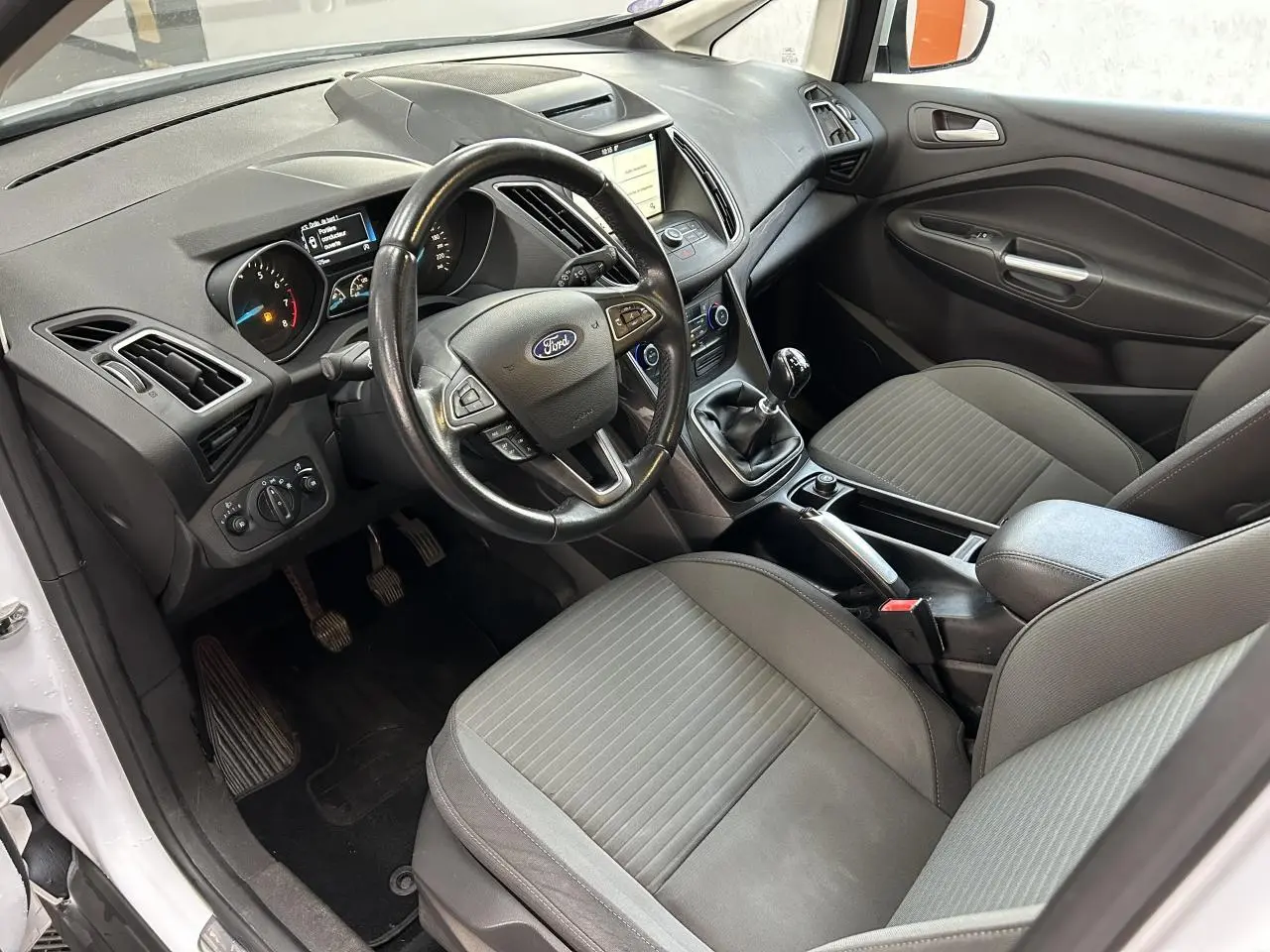 Intérieur avant du Ford C-MAX blanc 2018, vue côté conducteur montrant tableau de bord, volant et sièges gris.