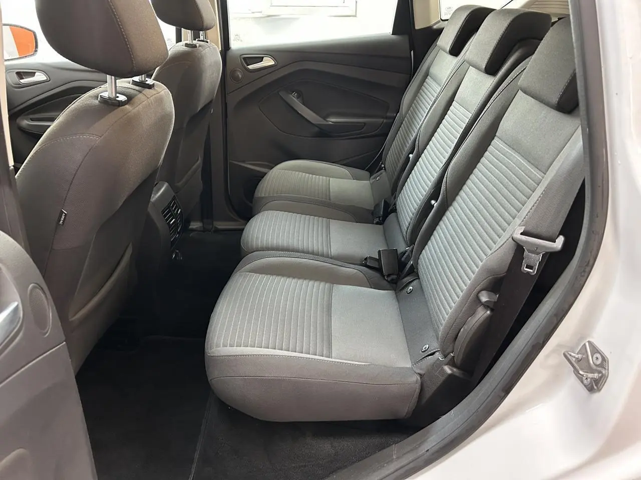 Vue latérale côté droit de l'habitacle arrière d'un Ford C-MAX blanc, sièges tissu gris et ceintures visibles.