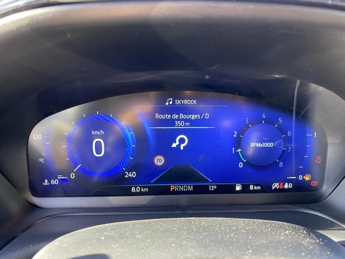 Vue rapprochée du tableau de bord numérique bleu du Ford Puma gris 2021, affichant vitesse, régime et navigation.