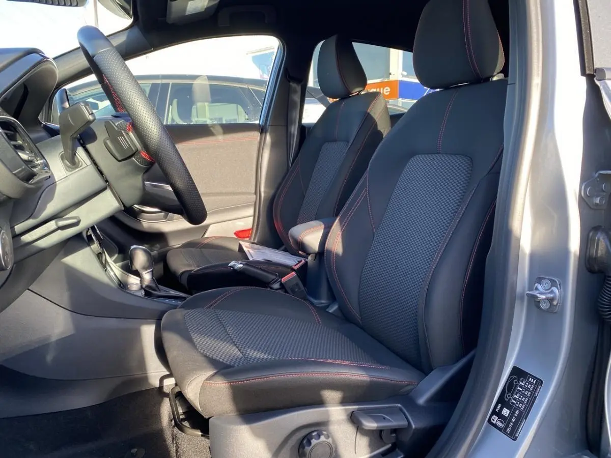 Vue intérieure côté conducteur du Ford Puma gris 2021, sièges tissu noir avec surpiqûres rouges et volant multifonctions.